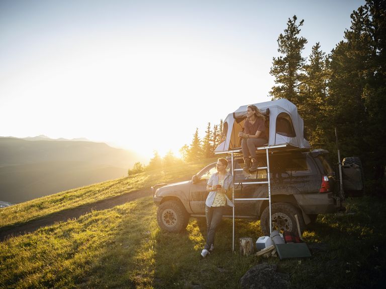 Couple camping, relaxing at SUV rooftop tent in sunny, idyllic field, Alberta, Canada