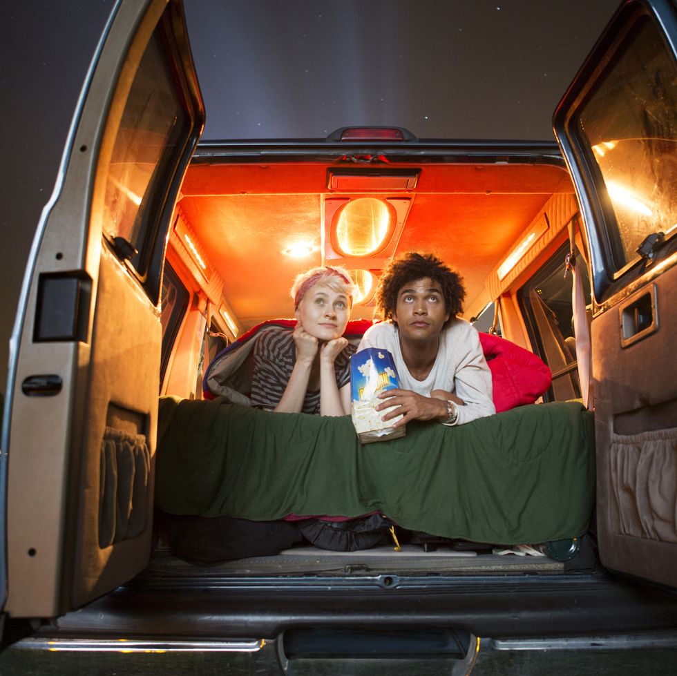 couple holding popcorn while sitting in camping van during drive in movie