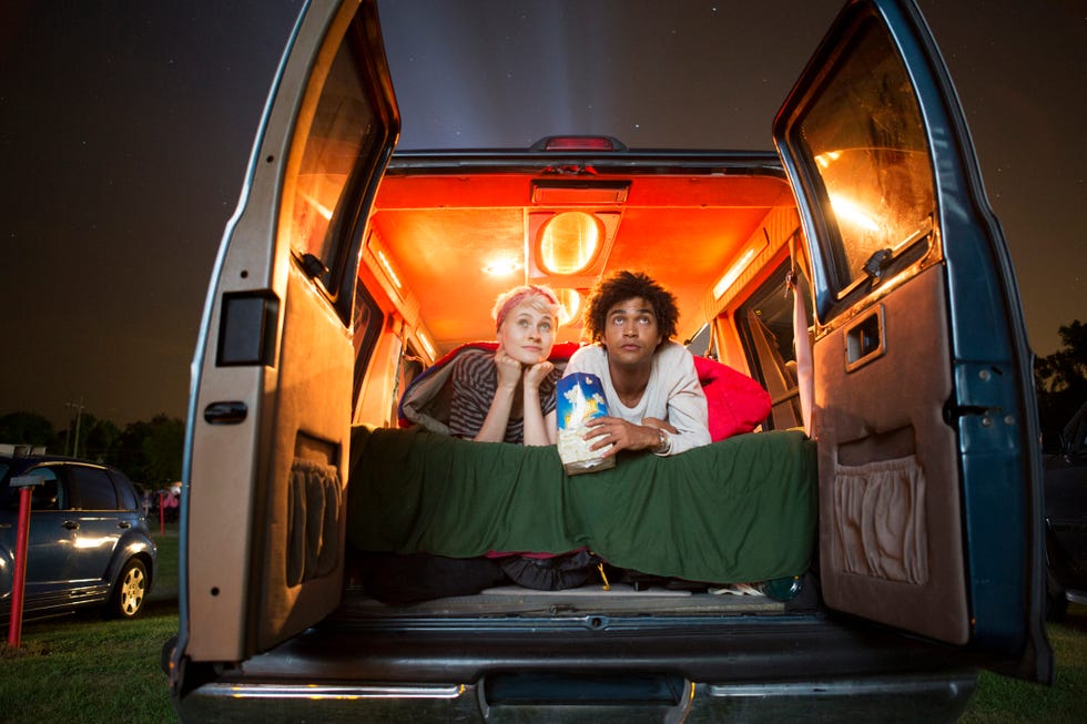 couple holding popcorn while sitting in camping van during drive in movie