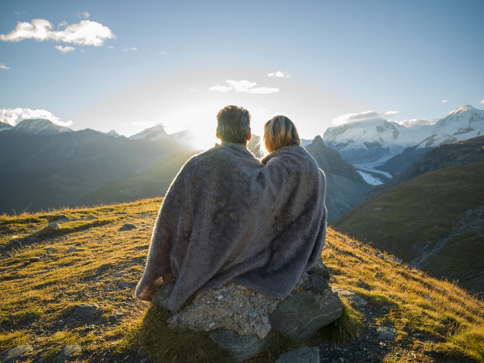 couple huddle in blanket, watch mountain sunrise