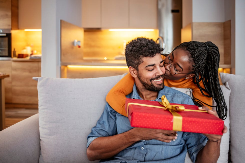 a woman hugging and kissing her partner and giving him a christmas gift