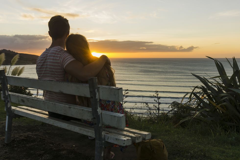couple in love sitting on bench looking at sunset