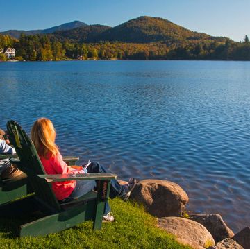 couple in wooden adirondack chairs watching over mirror lake in the adirondack mountains at lake placid, northern new york in the united states