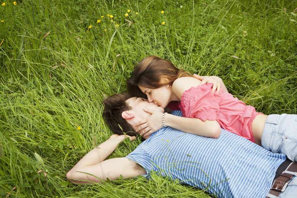 Couple kissing, laying in grass.
