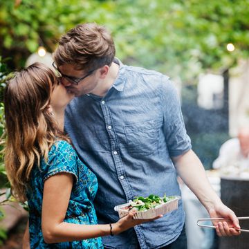 Couple Kissing While Cooking At Family BBQ