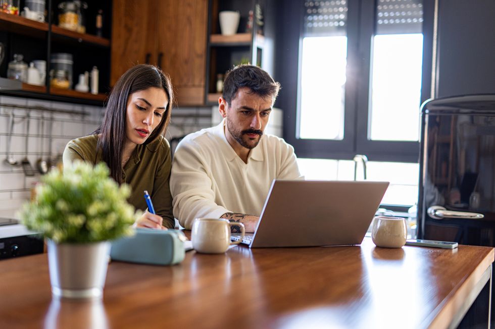 couple managing domestic finances using laptop and taking notes at home kitchen