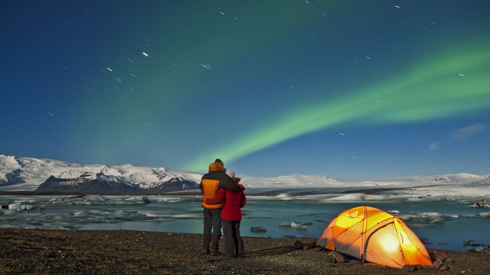 couple outside of their tent looking at northern lights in the sky