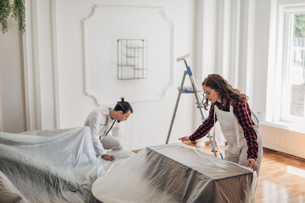 couple preparing for renovating, laying a plastic tarp over furniture