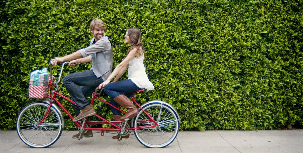 couple riding tandem bike in front of hedge