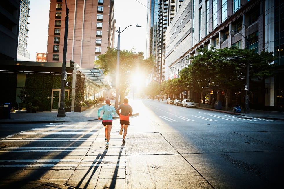 Couple running together on empty city street during workout at sunrise