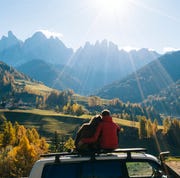 Couple sit on car rooftop looking at mountains in the distance couple sit on car rooftop looking at mountains in the distance