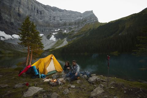 Couple sitting by campfire at remote mountain lakeside campsite