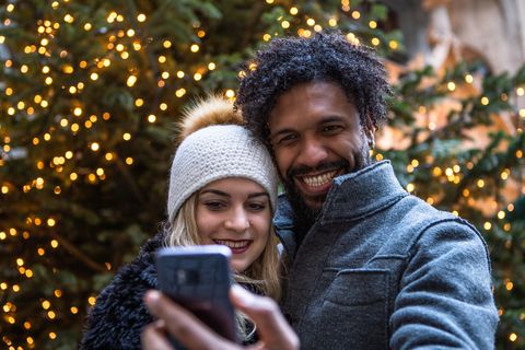 couple smiling while taking selfie against illuminated christmas tree