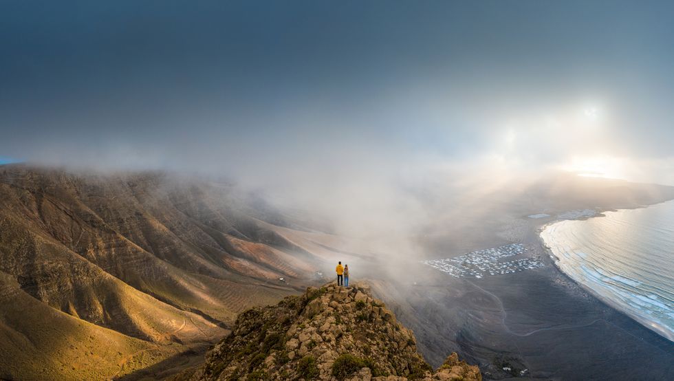 couple standing on top of a cliff looking at sunset, lanzarote, spain