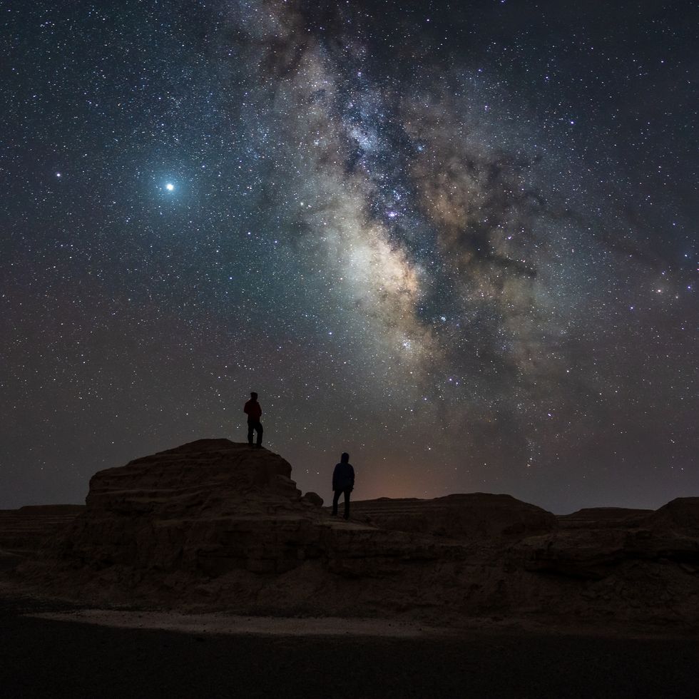a couple people standing on a rock with a starry sky above
