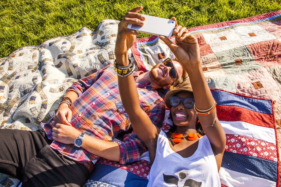 couple taking cell phone selfie on blanket in park