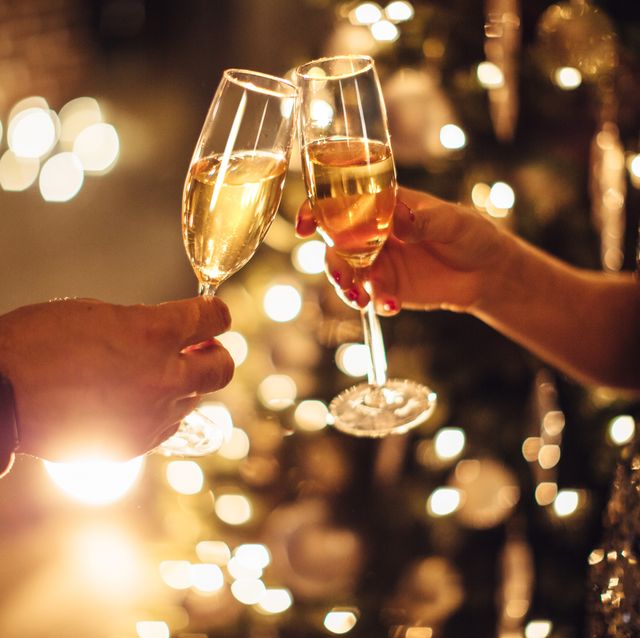 couple holding glasses of champagne in front of christmas tree toasting to each other evening or night