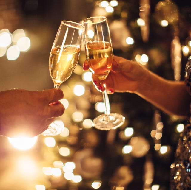 couple holding glasses of champagne in front of christmas tree toasting to each other evening or night