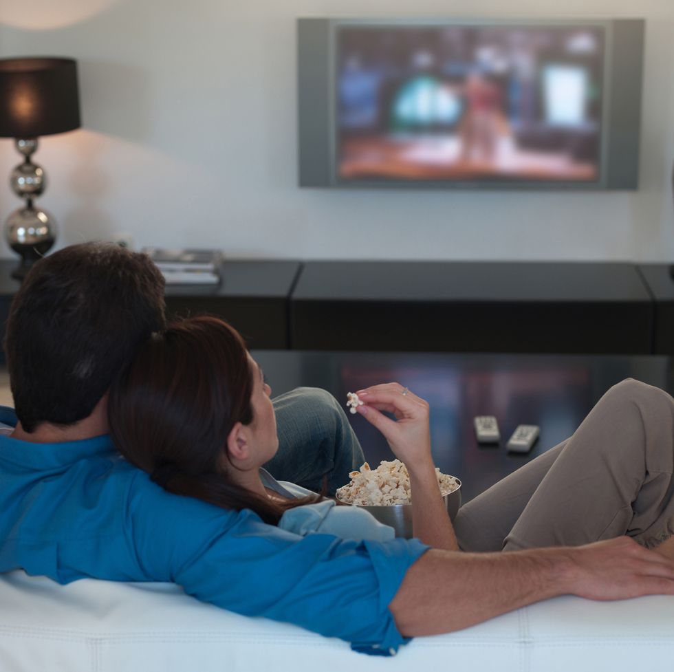 staycation ideas - Couple watching television together and eating popcorn