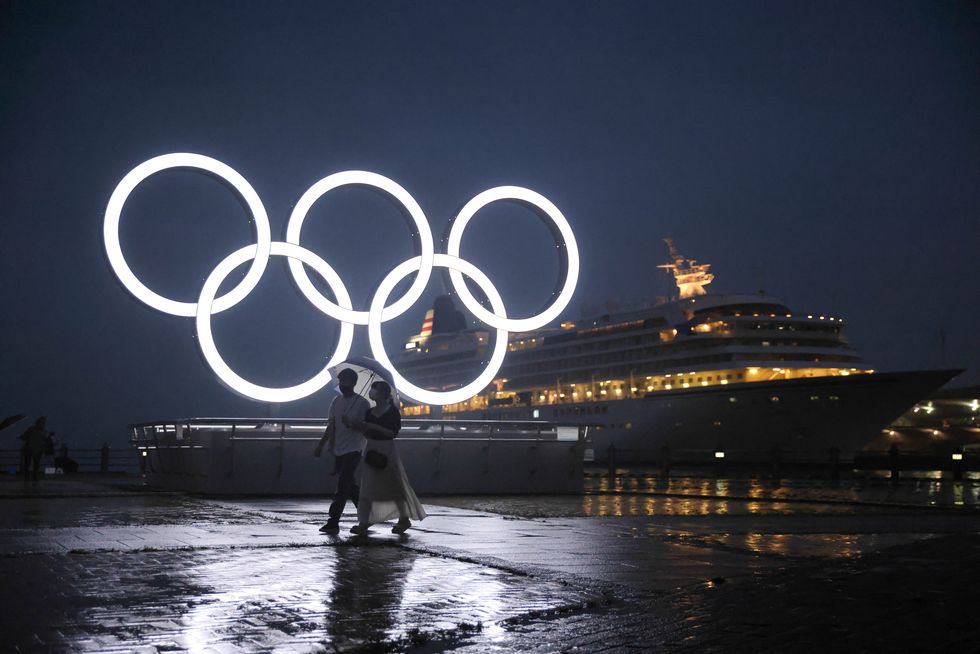 a couple with an umbrella walks past the illuminated olympic