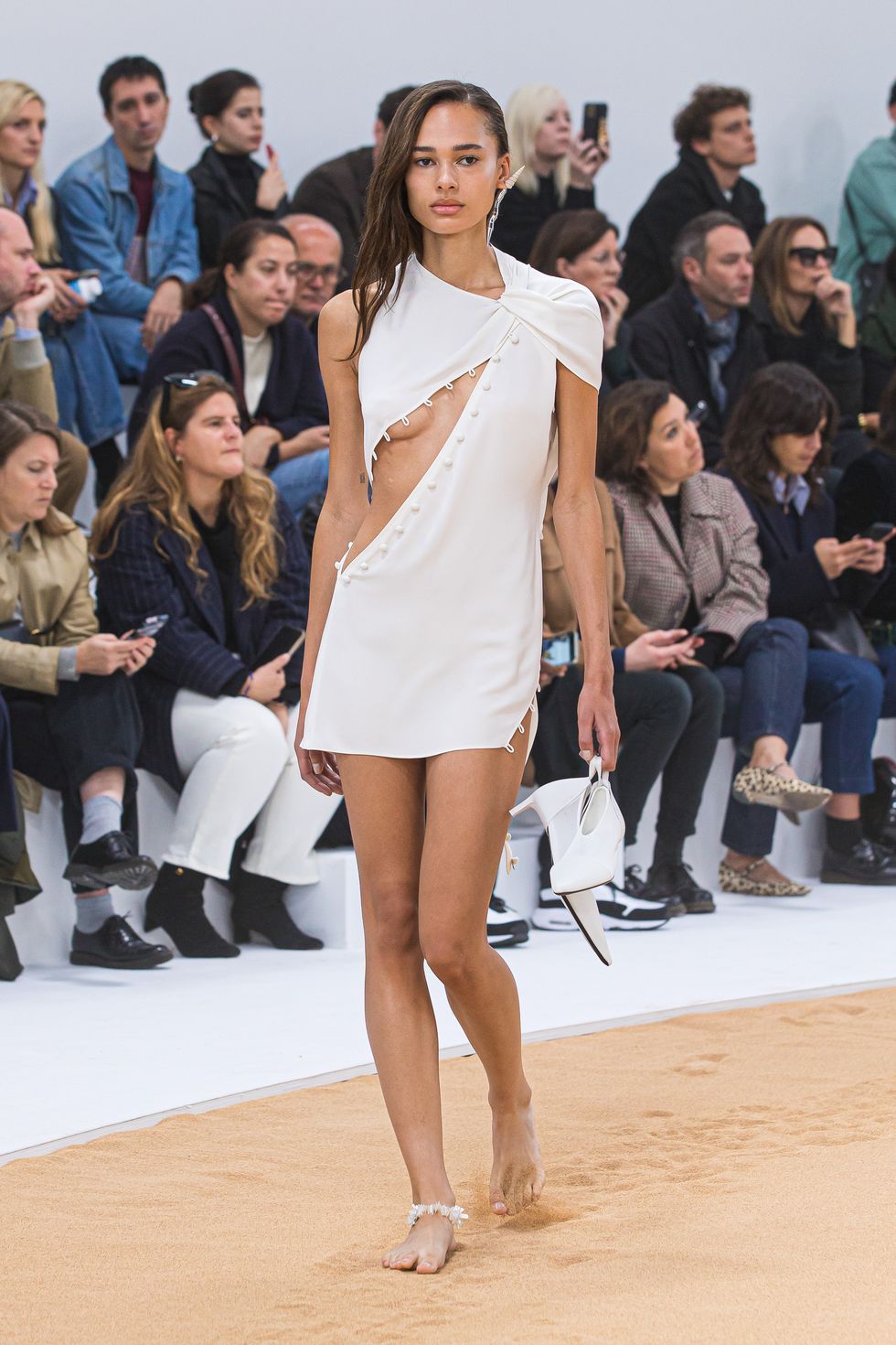 a model at the ﻿courrèges show while holding her slingbacks on a runway made of sand﻿