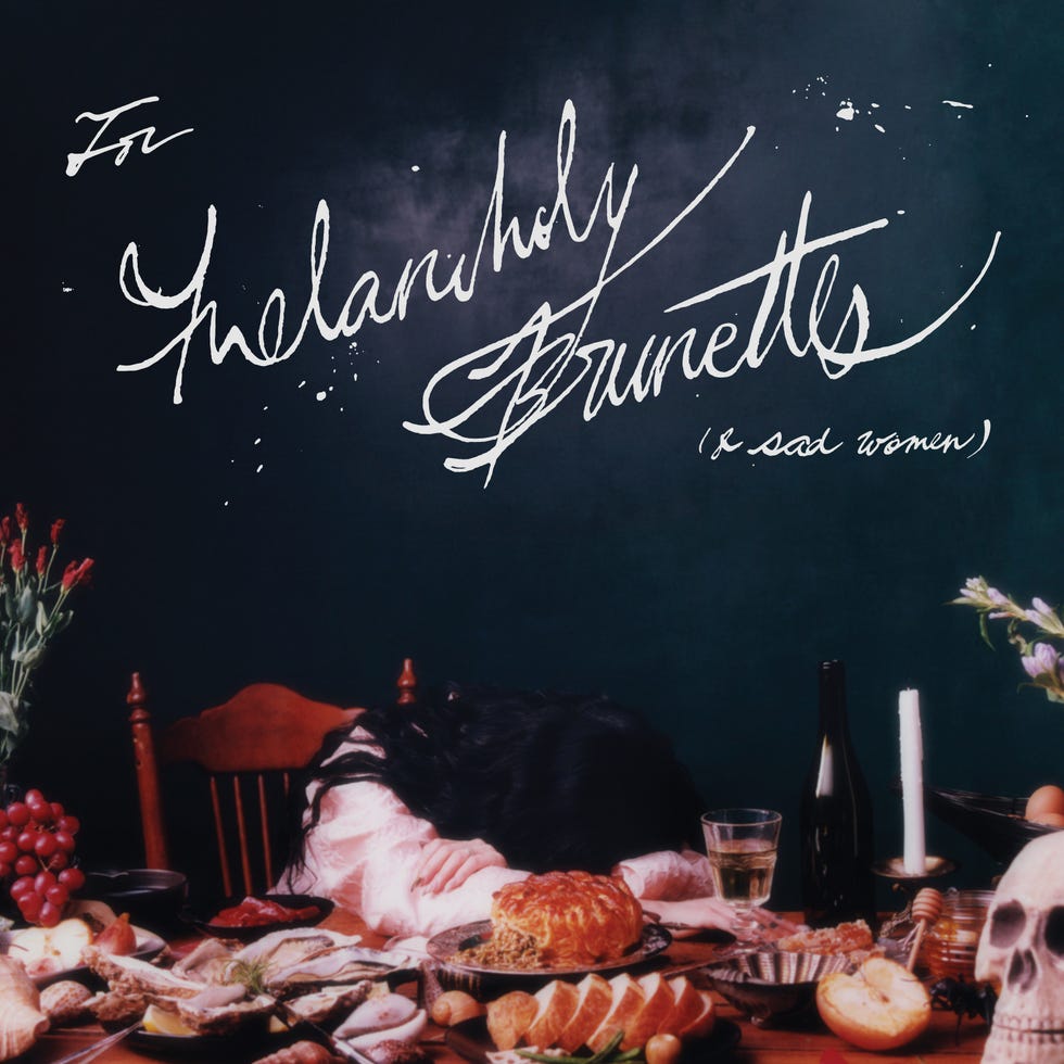 a table laden with food next to a woman with her head down conveying themes of melancholy
