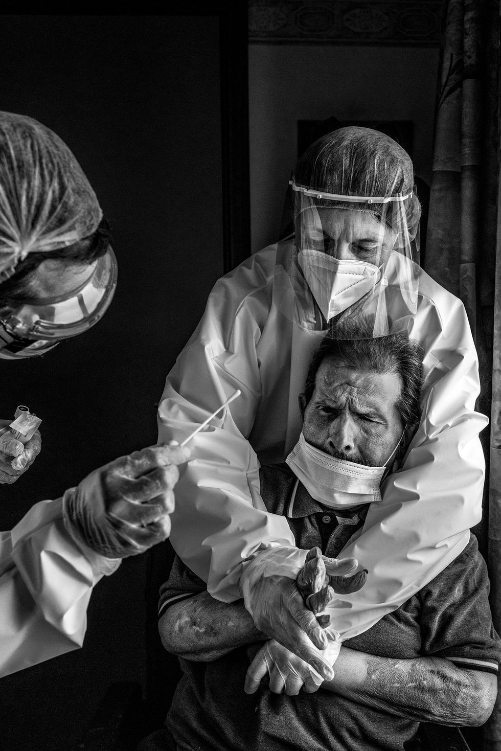 In een verpleeghuis in het Belgische La Louvire houdt een verpleegster een bewoner stevig vast zodat haar collega speeksel voor een COVID19test bij de man kan afnemen Verpleeghuizen behoren tot de plekken die het zwaarst door de pandemie zijn getroffen
