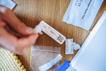 a woman squeezing the sample liquid on a test strip while carrying out a covid 19 rapid self test at home