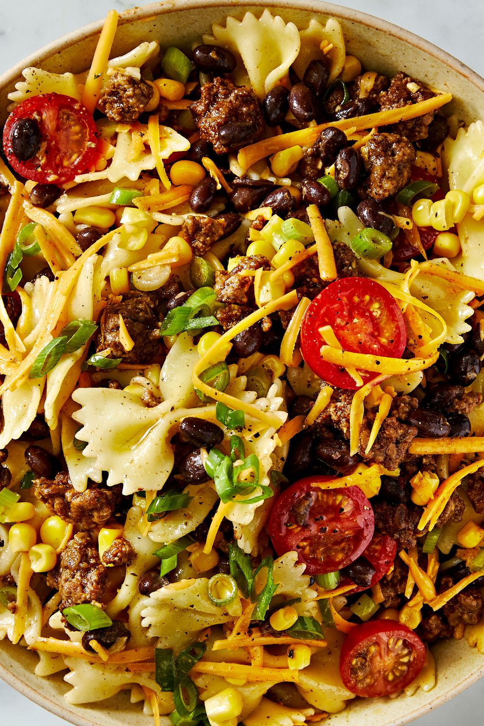 cowboy pasta salad with halved cherry tomatoes, ground beef, black beans, sliced scallions, and shredded cheddar