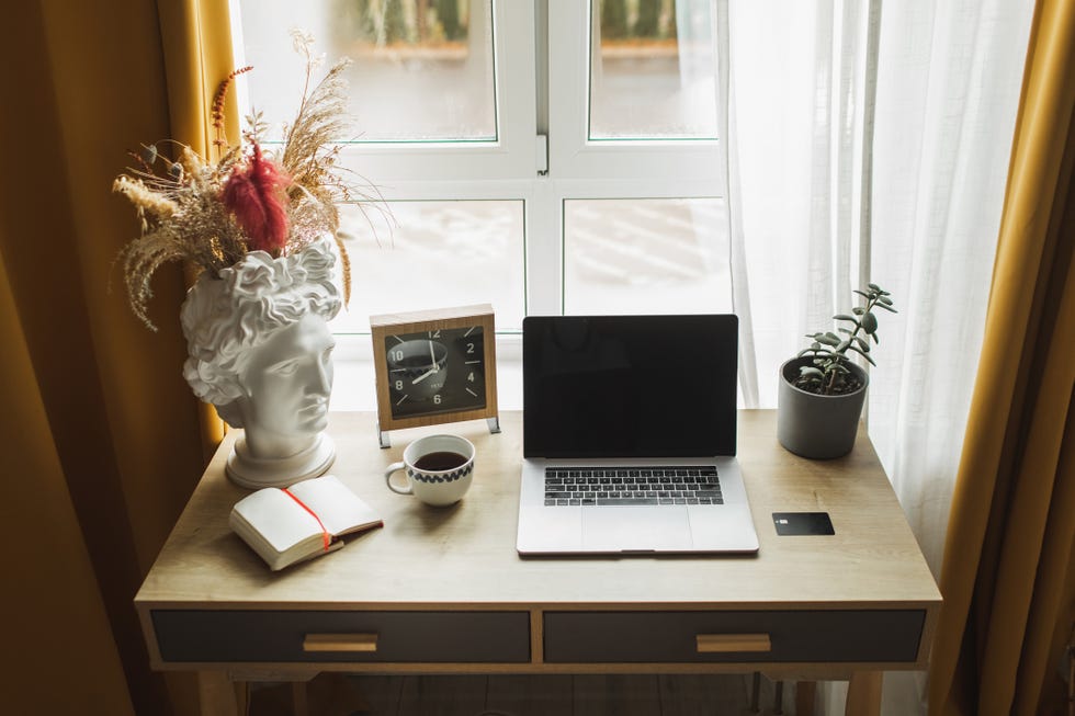 cozy and stylish workplace at home laptop on table, hot coffee, decorative vase, house plant and curtains on window