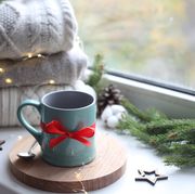 cozy home picture of blue ceramic cup with coffee on window sill, christmas decorations, warm knitted sweaters and pine tree green branches in background