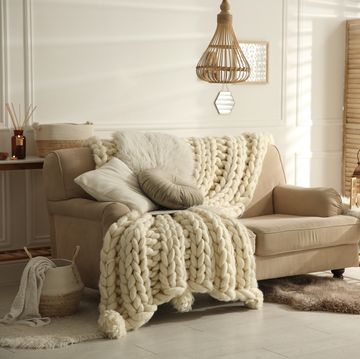 cozy living room interior with beige sofa, knitted blanket and cushions