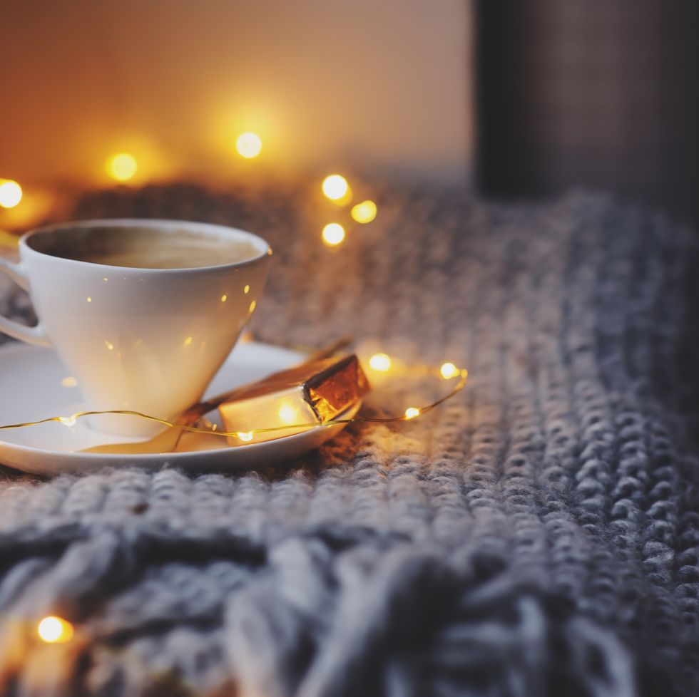 cozy winter or autumn morning at home hot coffee with gold metallic spoon, warm blanket, garland and candle lights, swedish hygge concept