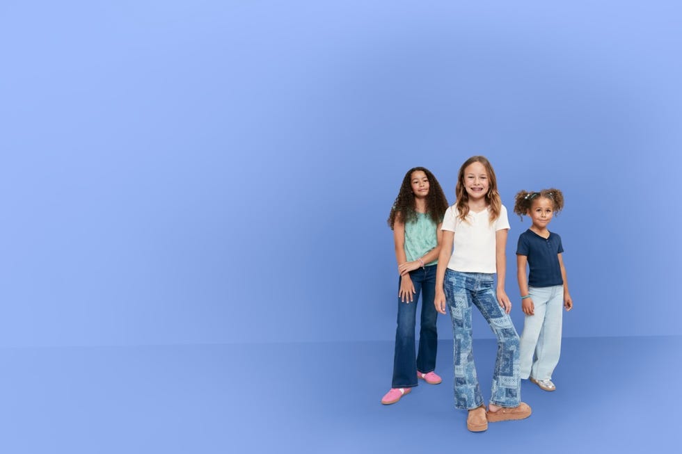 three children posing against a solid blue background wearing casual outfits