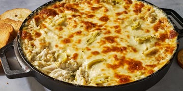 crab and artichokes in a cheesy baked dip in a cast iron dip served with toasted bread
