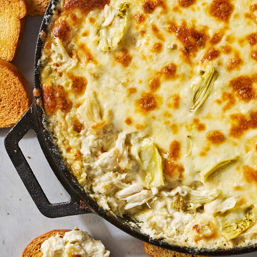 crab and artichokes in a cheesy baked dip in a cast iron dip served with toasted bread
