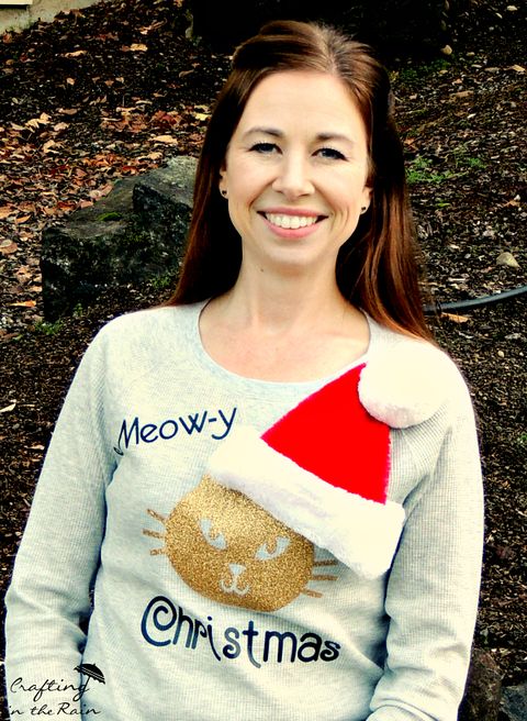 woman in sweater with a gold cat's face wearing a real santa hat that is glued to the sweater the sweater reads meowy christmas