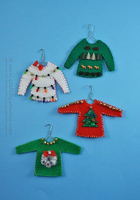 christmas tree ornaments shaped like ugly christmas sweaters on hangers, with a green one with a wreath, a red one with a tree, a white one with lights, and a green one with trees and moose