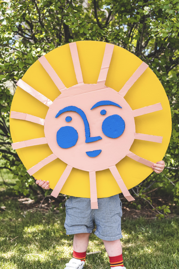 crafts for kids, child holding a large diy smiling sun made of cardboard outdoors