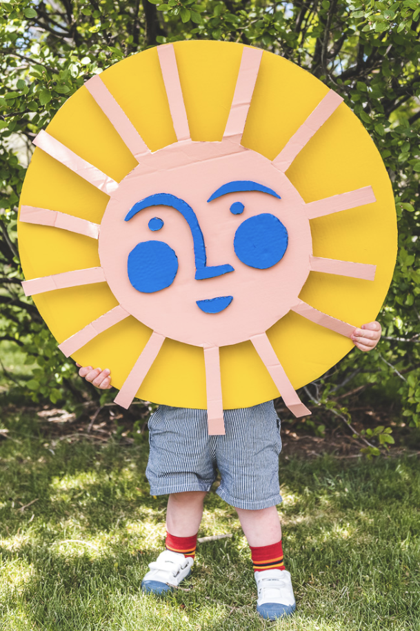 crafts for kids, child holding a large diy smiling sun made of cardboard outdoors