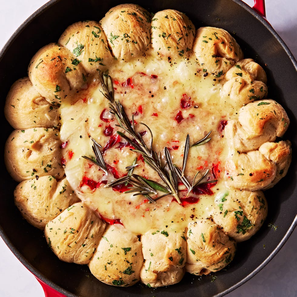 brie dip in a cast iron skillet swirled with cranberry sauce and surrounded by herby biscuits