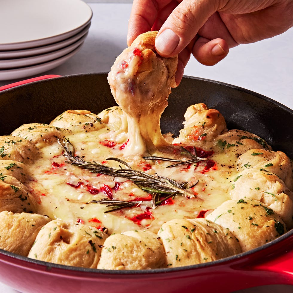 brie dip in a cast iron skillet swirled with cranberry sauce and surrounded by herby biscuits