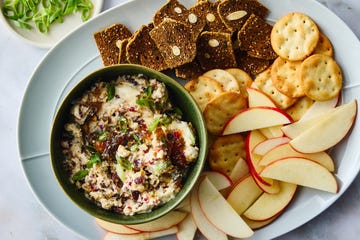 a platter featuring a green bowl of spread accompanied by crackers apple slices and a small dish of chopped green onions