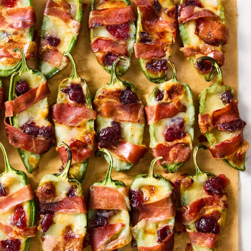 jalapeños stuffed with brie and wrapped with bacon, topped with cranberry sauce on a sheet tray