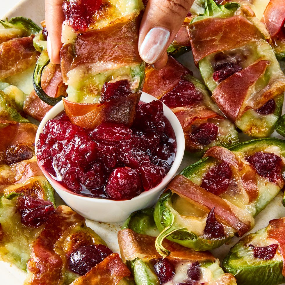 jalapeños stuffed with brie and wrapped with bacon, topped with cranberry sauce on a sheet tray