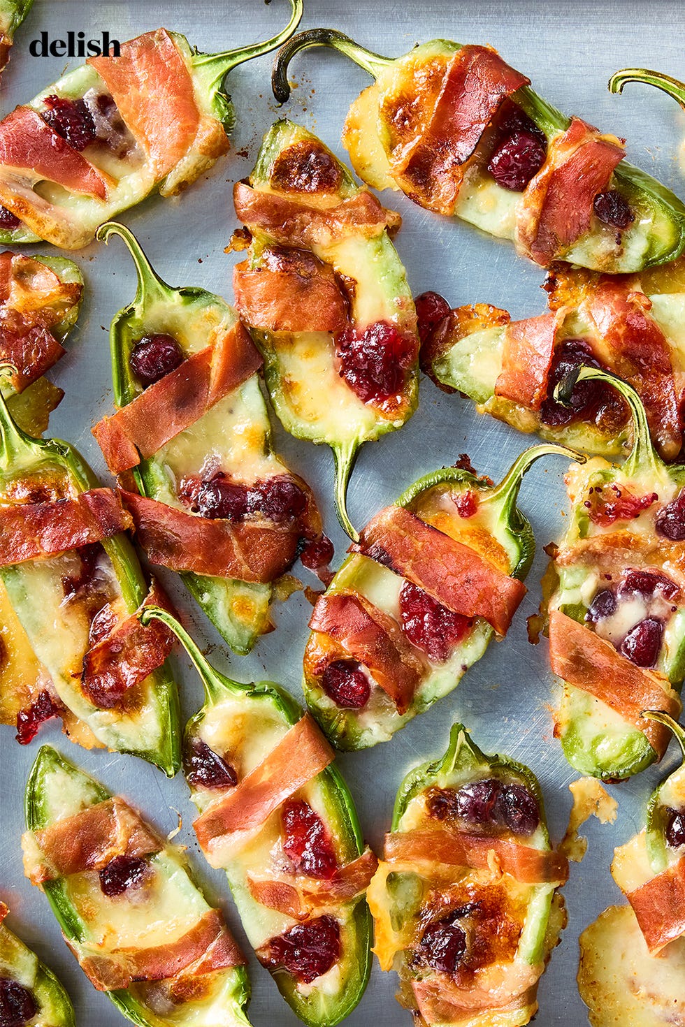 jalapeños stuffed with brie and wrapped with bacon, topped with cranberry sauce on a sheet tray