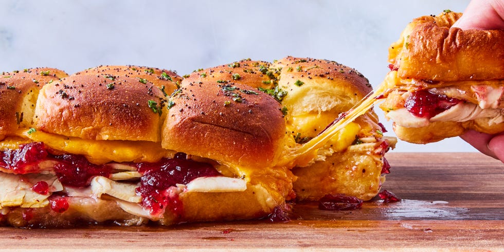 sliders filled with sliced turkey, cranberry sauce, and cheese topped with a poppyseed butter topping