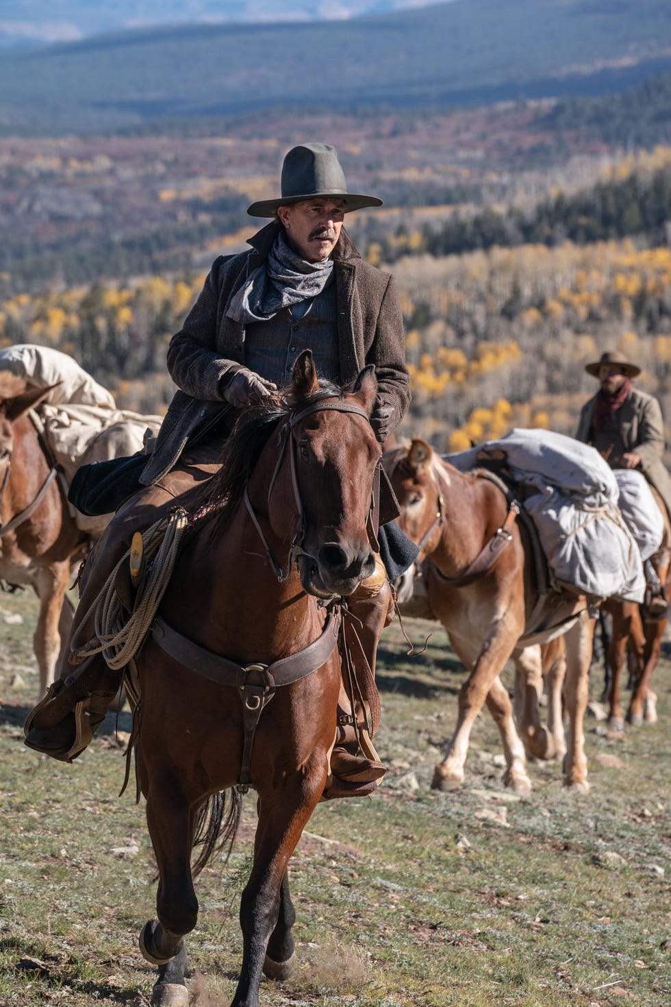 cowboy riding a horse with pack horses in the background