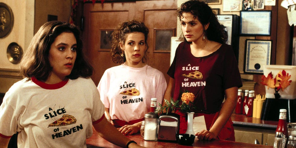 three individuals wearing matching restaurant uniforms stand behind a counter