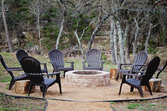 black adirondack chairs and log side tables encircling a diy outdoor stone fire pit